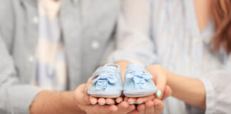 Husband and pregnant woman holding baby shoes, closeup